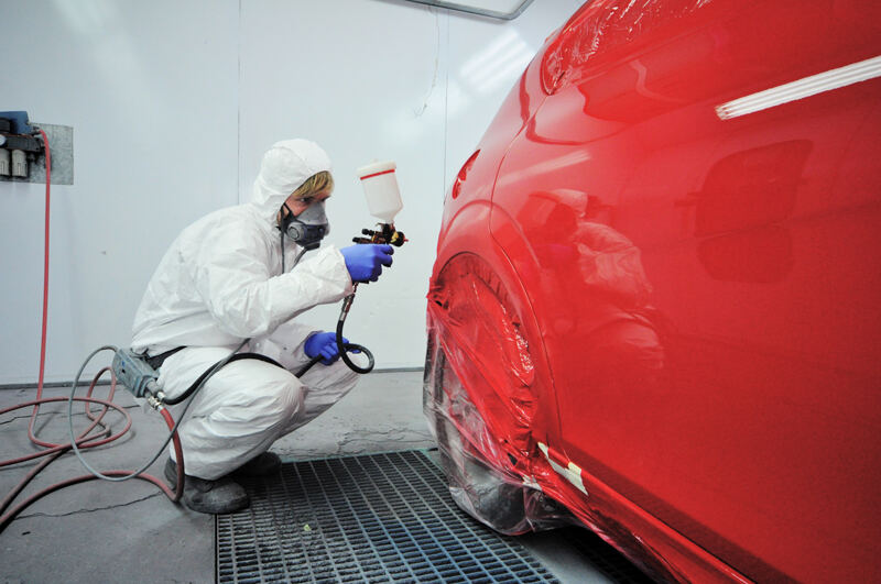 Painter spraying a red car in the spray booth